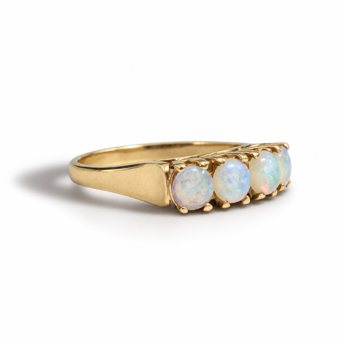 A yellow gold ring featuring four round, iridescent white opal gemstones in a row, set in a prong setting on a polished gold band, photographed on a clean white background.