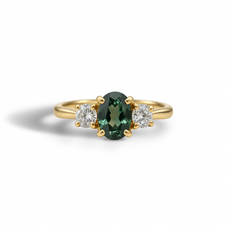 A yellow gold three-stone ring featuring a central oval-cut dark green gemstone flanked by two round-cut clear stones, set against a clean white background.