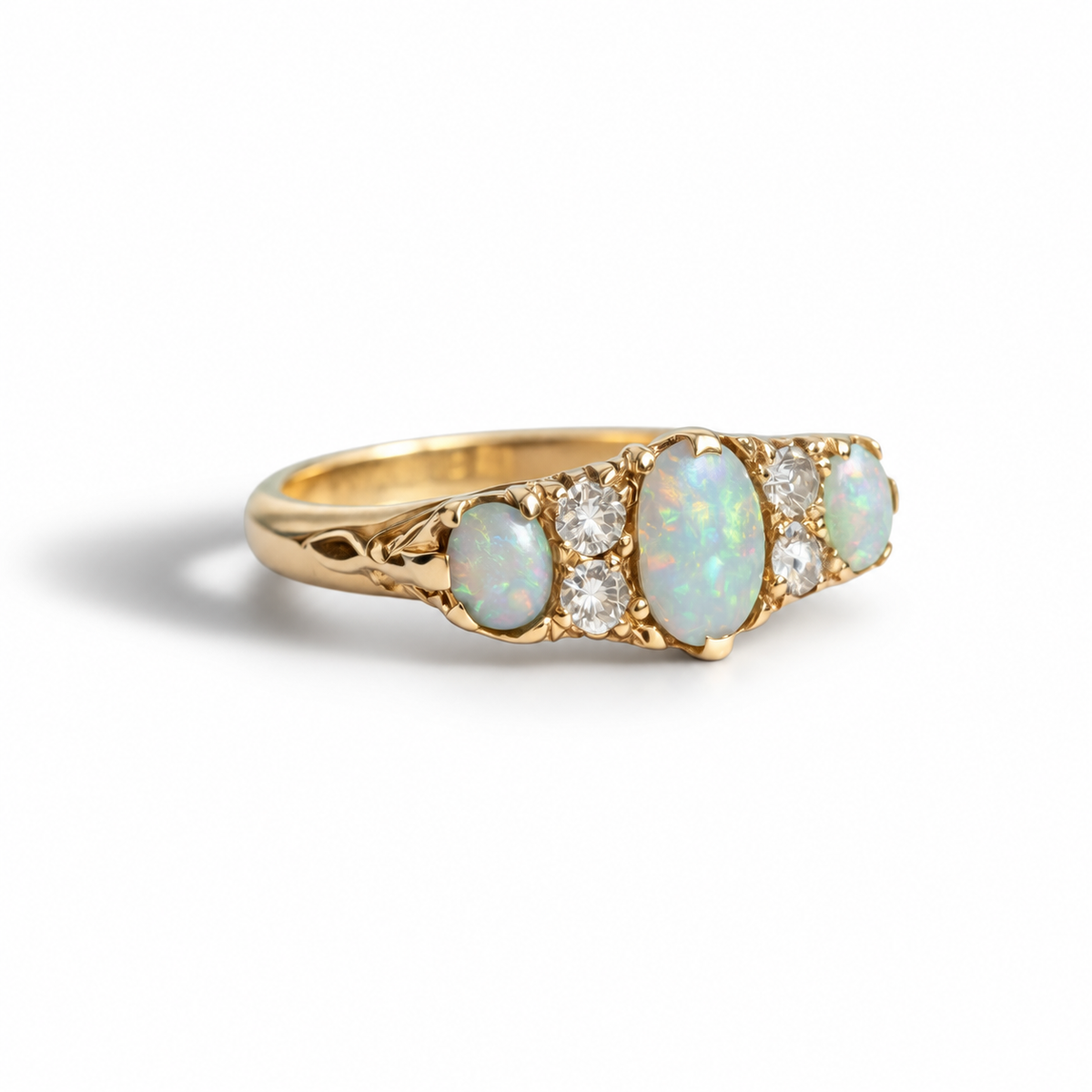 A yellow gold ring featuring a row of five oval opal and round clear gemstone accents, photographed on a clean white background.