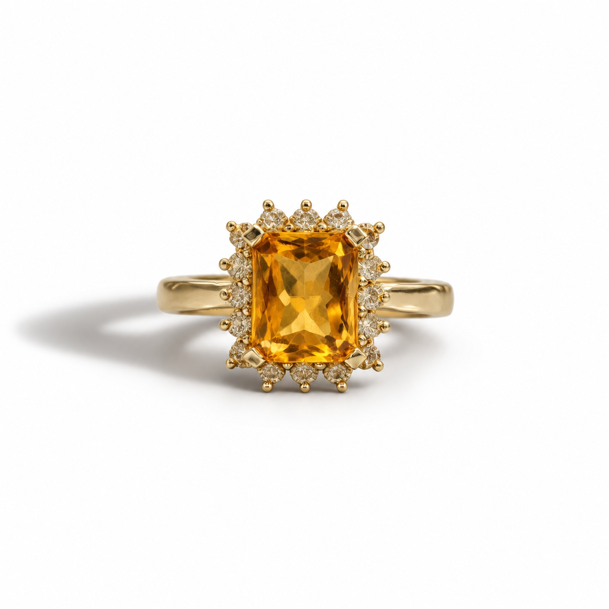 A yellow gold ring featuring a large rectangular emerald-cut  citrine orange gemstone in a prong setting, surrounded by a halo of small round diamonds, shown on a clean white background.