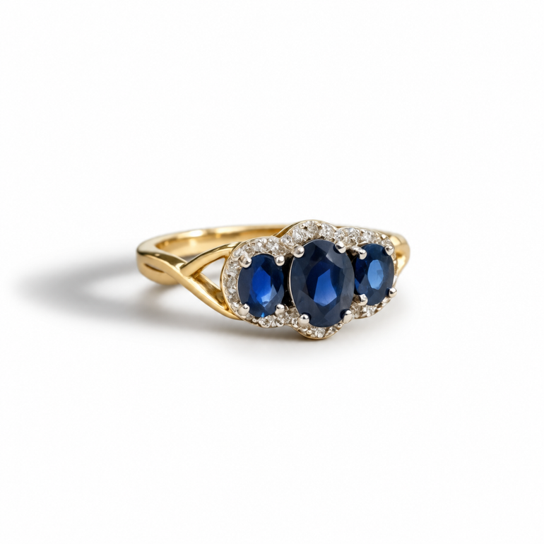 A yellow gold ring featuring three oval-cut deep blue sapphires in a halo setting with small clear stones, shown on a clean white background.