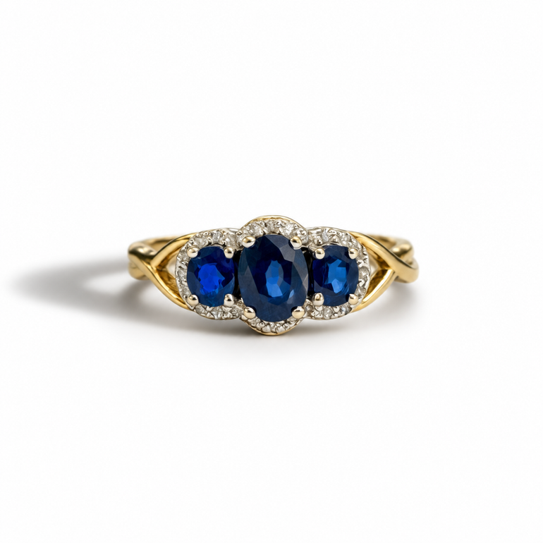 A yellow gold ring featuring three oval-cut deep blue sapphires in a pavé setting with small clear stones, photographed on a clean white background.