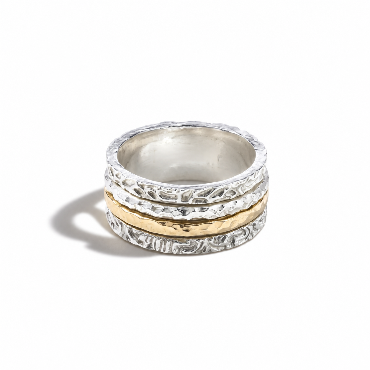 A stack of three textured rings, featuring two silver rings with floral engravings and one central gold ring, displayed on a clean white background.
