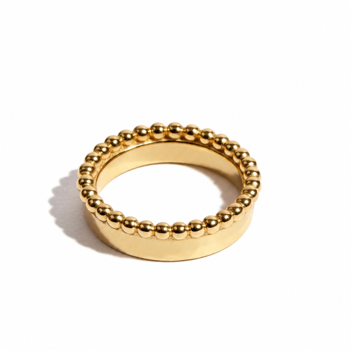 A gold beaded ring with a wide flat band, photographed on a clean white background with a soft shadow.
