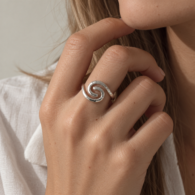 A close-up of a person's hand wearing a polished silver spiral ring, with her face partially visible in the upper right and a white shirt in the background.