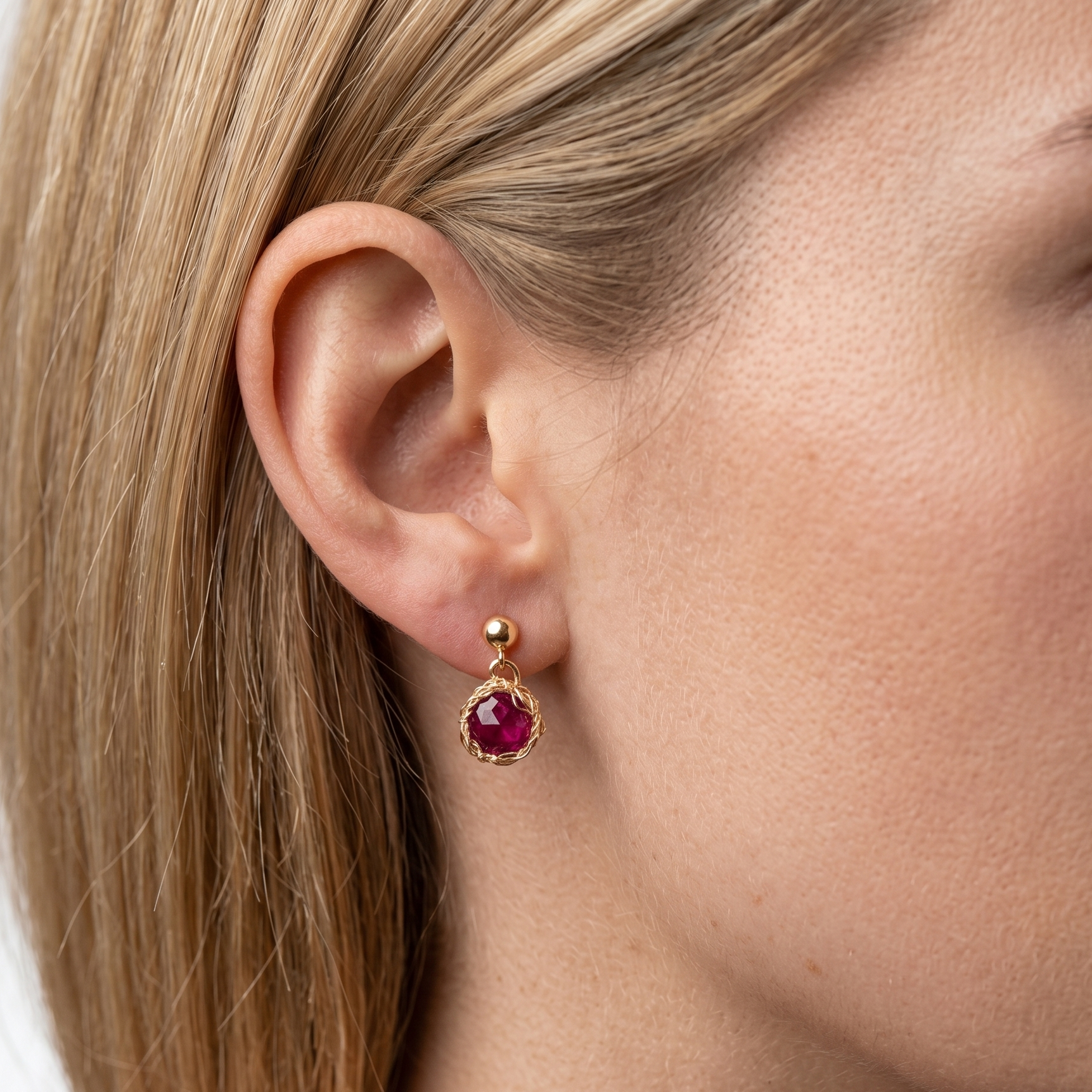 Close-up of a woman wearing gold earrings with red gemstones on a white background