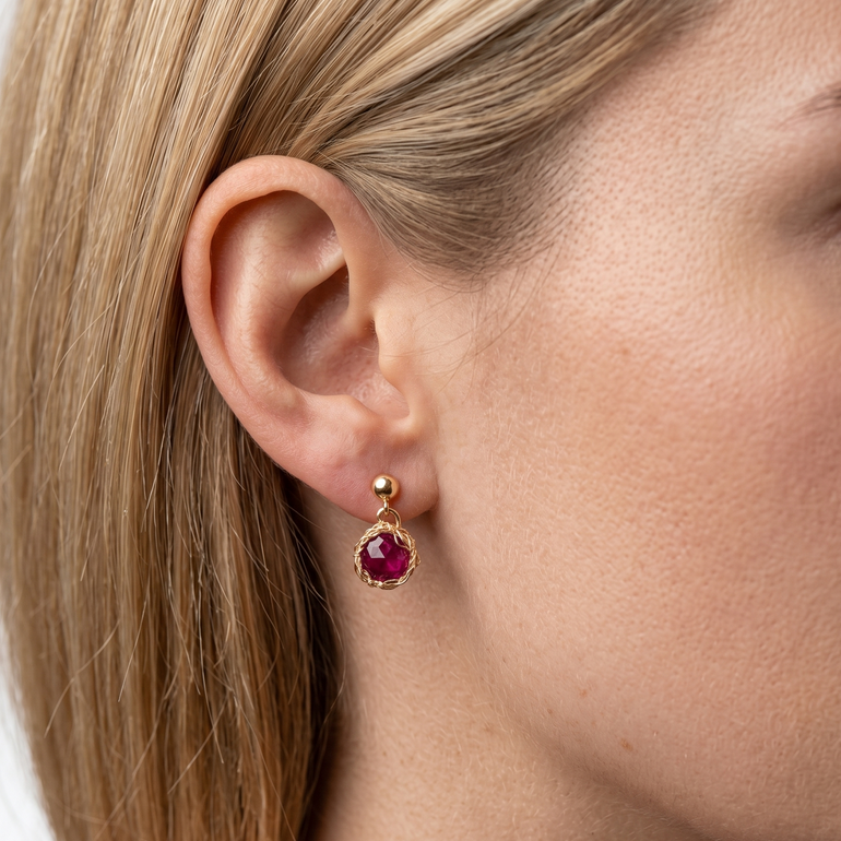 Close-up of a woman wearing gold earrings with red gemstones on a white background