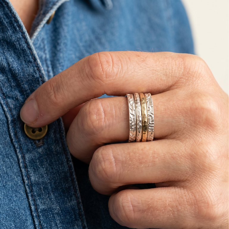 Hand wearing three gold rings with a blue denim background