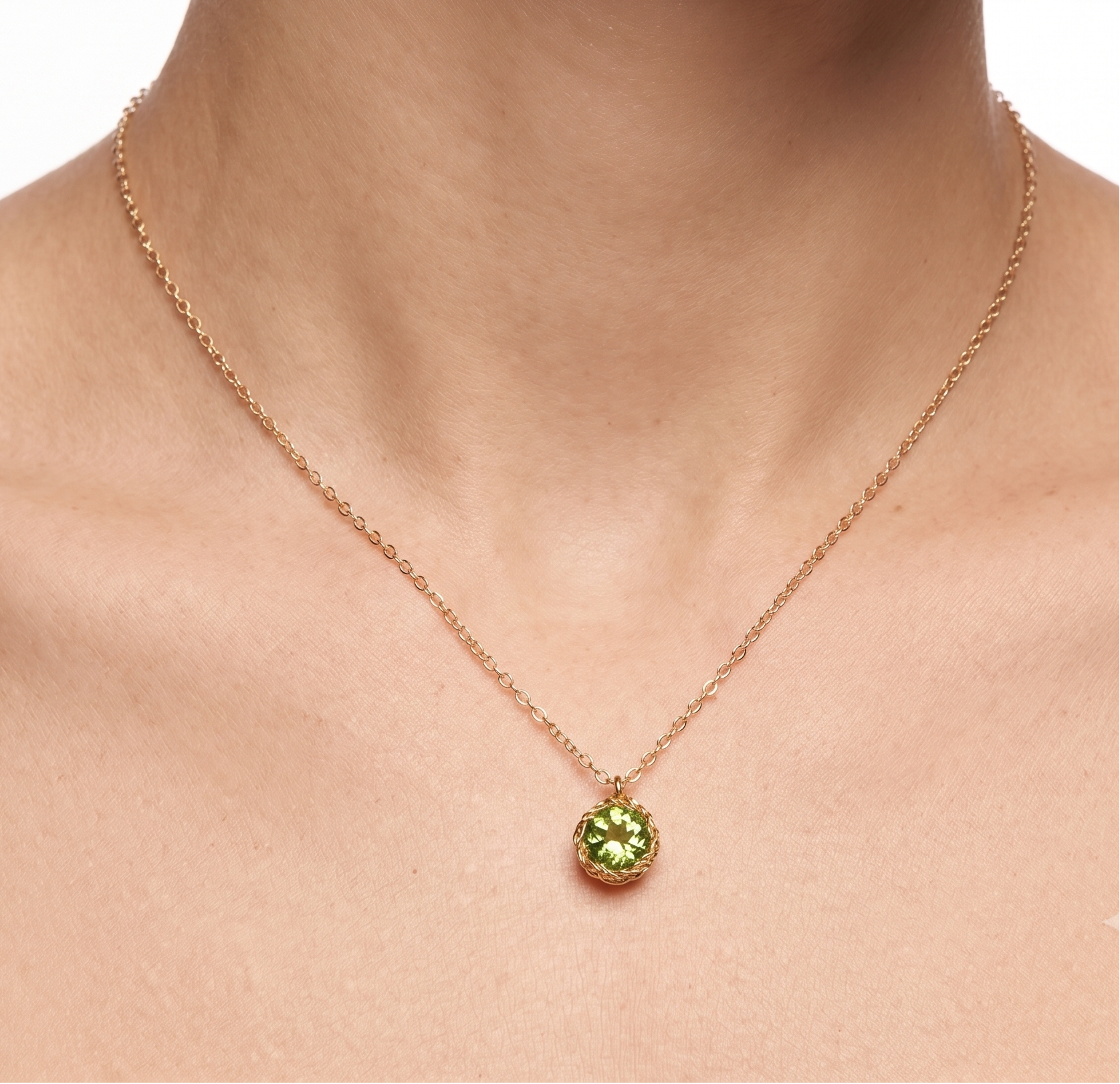 Gold necklace with a green pendant on a person's neck against a white background