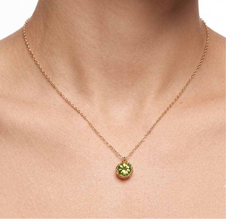 Gold necklace with a green pendant on a person's neck against a white background