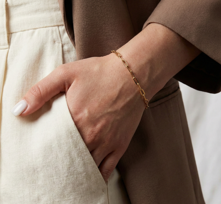 Close-up of a hand wearing a gold link bracelet with a neutral background