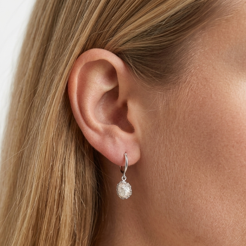 Close-up of a person wearing a silver earring with a clear gemstone.