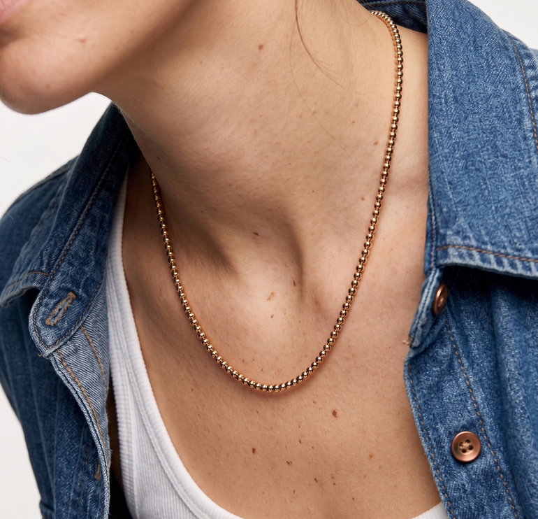 Person wearing a gold necklace with a denim jacket and white top