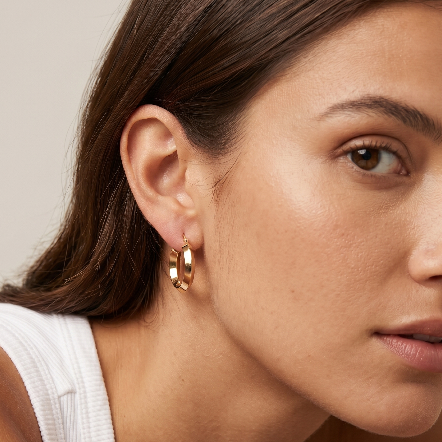 Close-up of a woman wearing gold hoop earrings with a neutral background