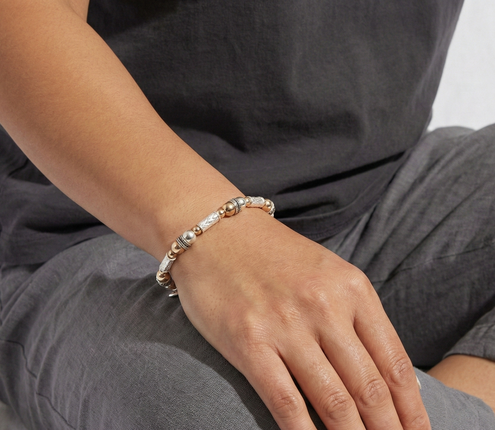Person wearing a  silver and gold beaded bracelet on a neutral background