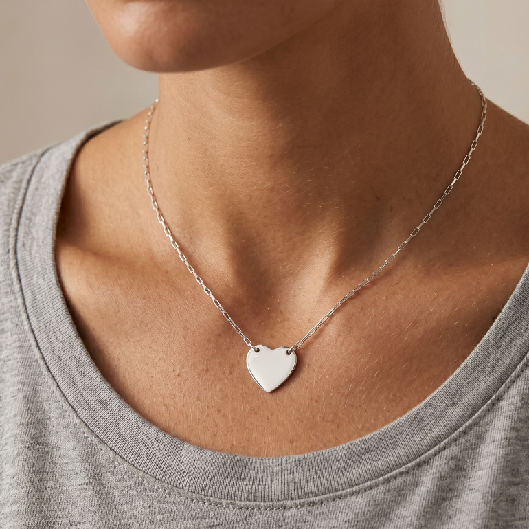 Person wearing a silver heart-shaped necklace on a neutral background