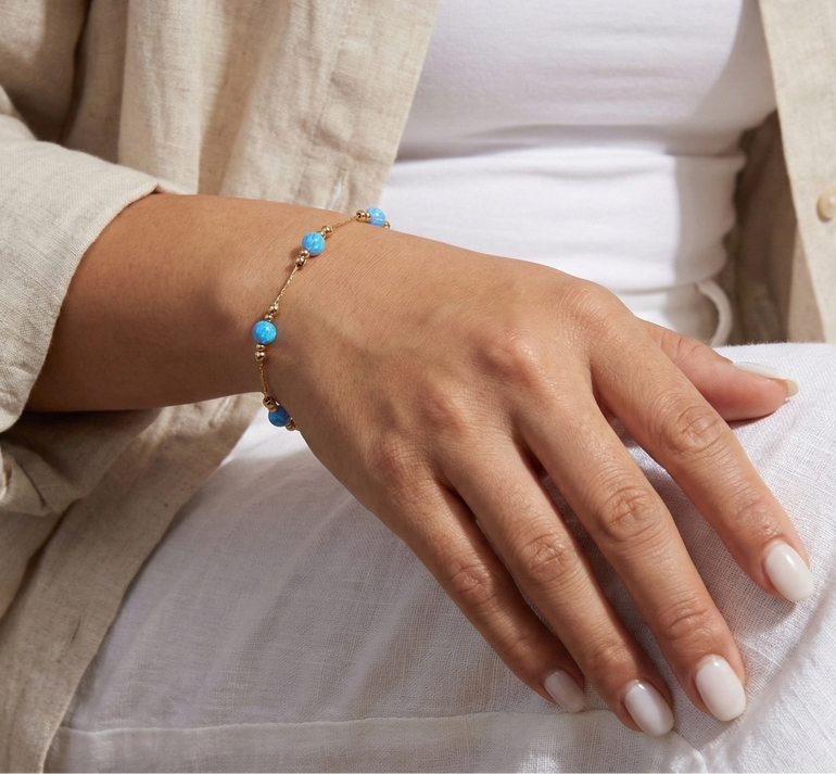 Hand wearing a turquoise beaded bracelet on a neutral background