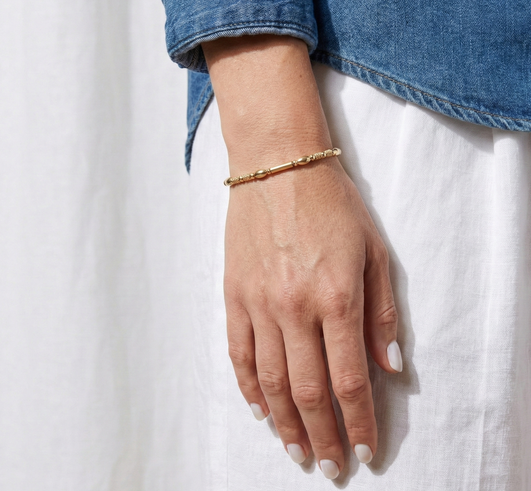 Hand wearing a gold bracelet on a white background