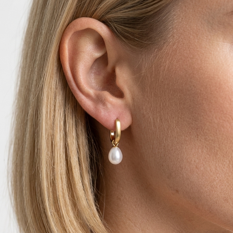 Gold hoop earring with a pearl on a blurred background