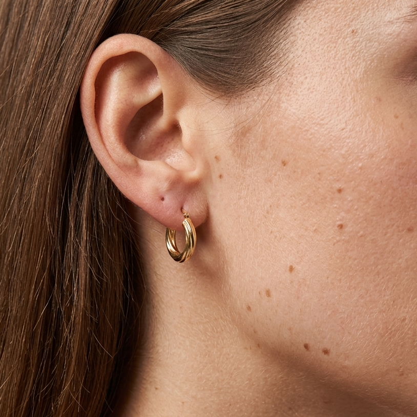 Close-up of a person wearing a gold hoop earring with a neutral background