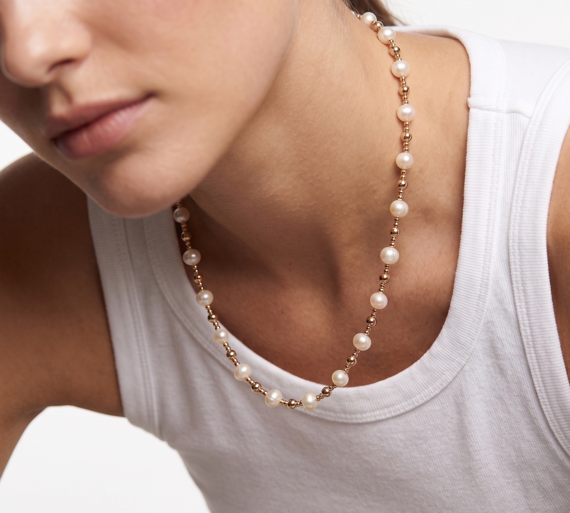 Close-up of a woman wearing a pearl necklace with a white tank top.