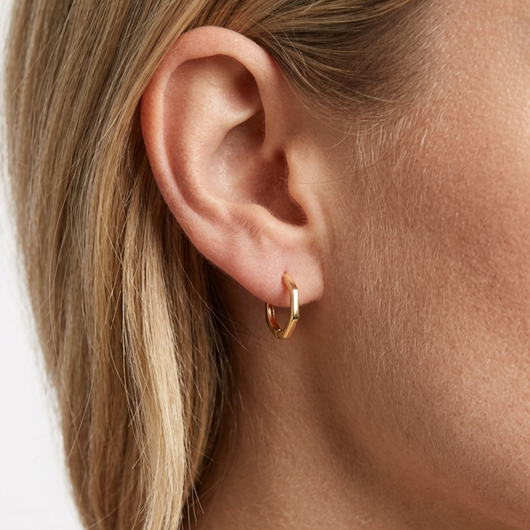 Close-up of a person wearing a gold hoop earring on a plain background