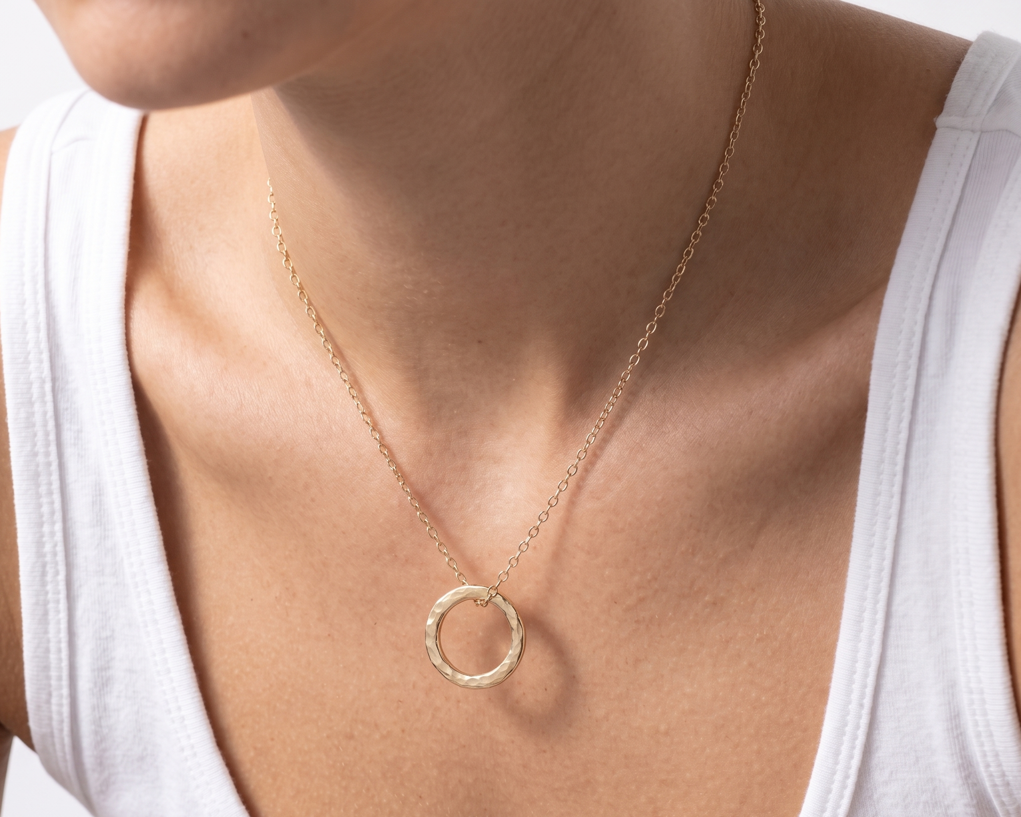 Gold necklace with a circular pendant worn by a person in a white tank top.