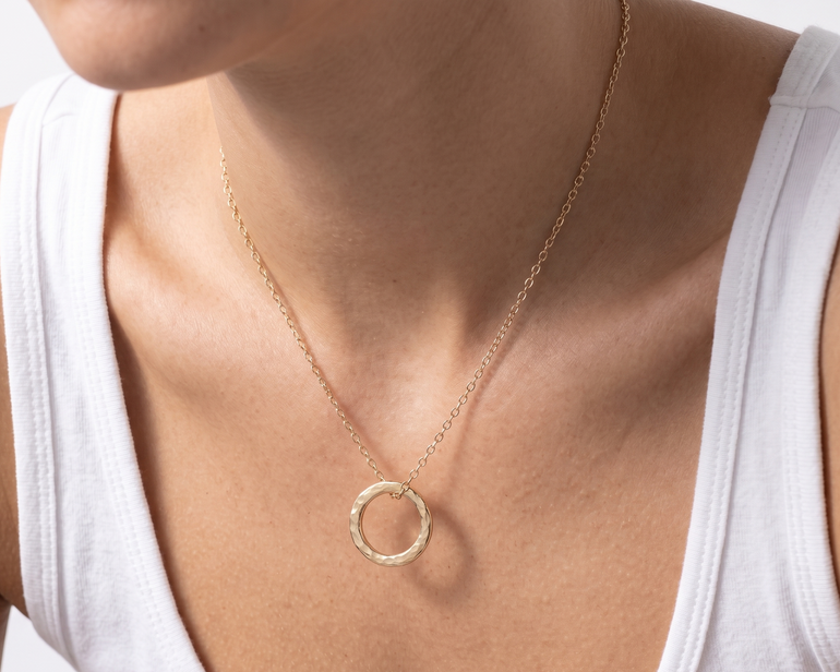 Gold necklace with a circular pendant worn by a person in a white tank top.