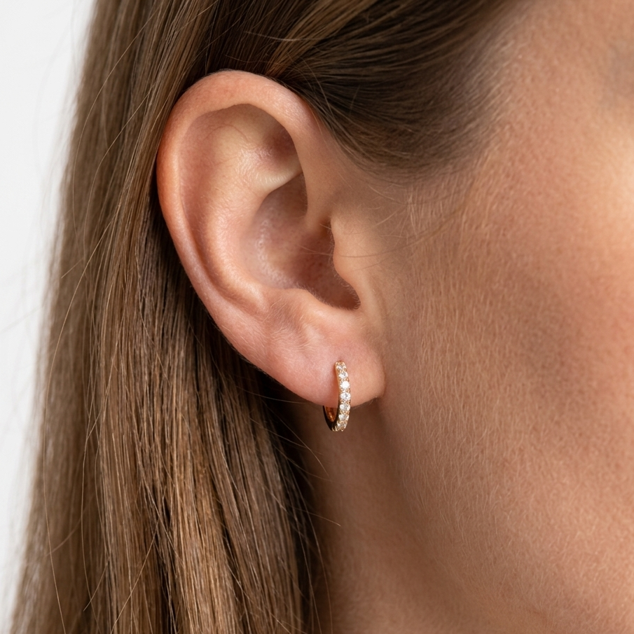 Close-up of an ear wearing a small hoop earring with a neutral background