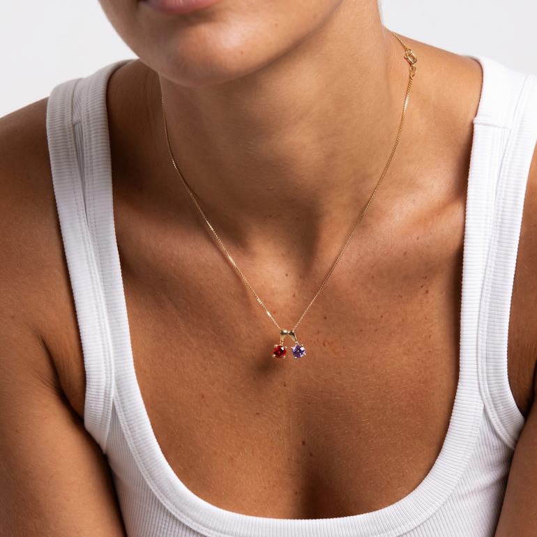 Close-up of a person wearing a gold necklace with colorful pendant on a plain background