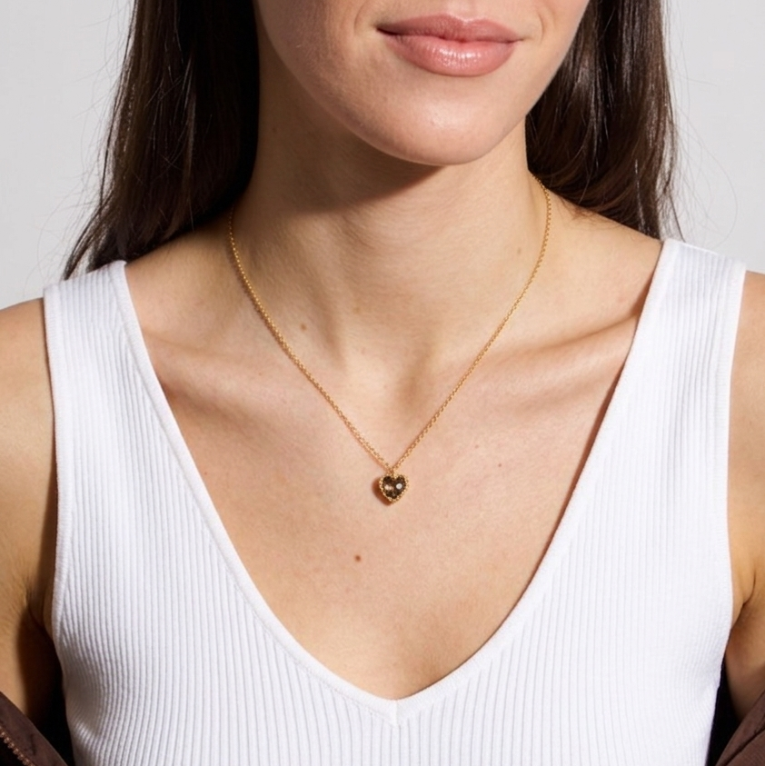 Woman wearing a white tank top and a gold necklace with a heart pendant.