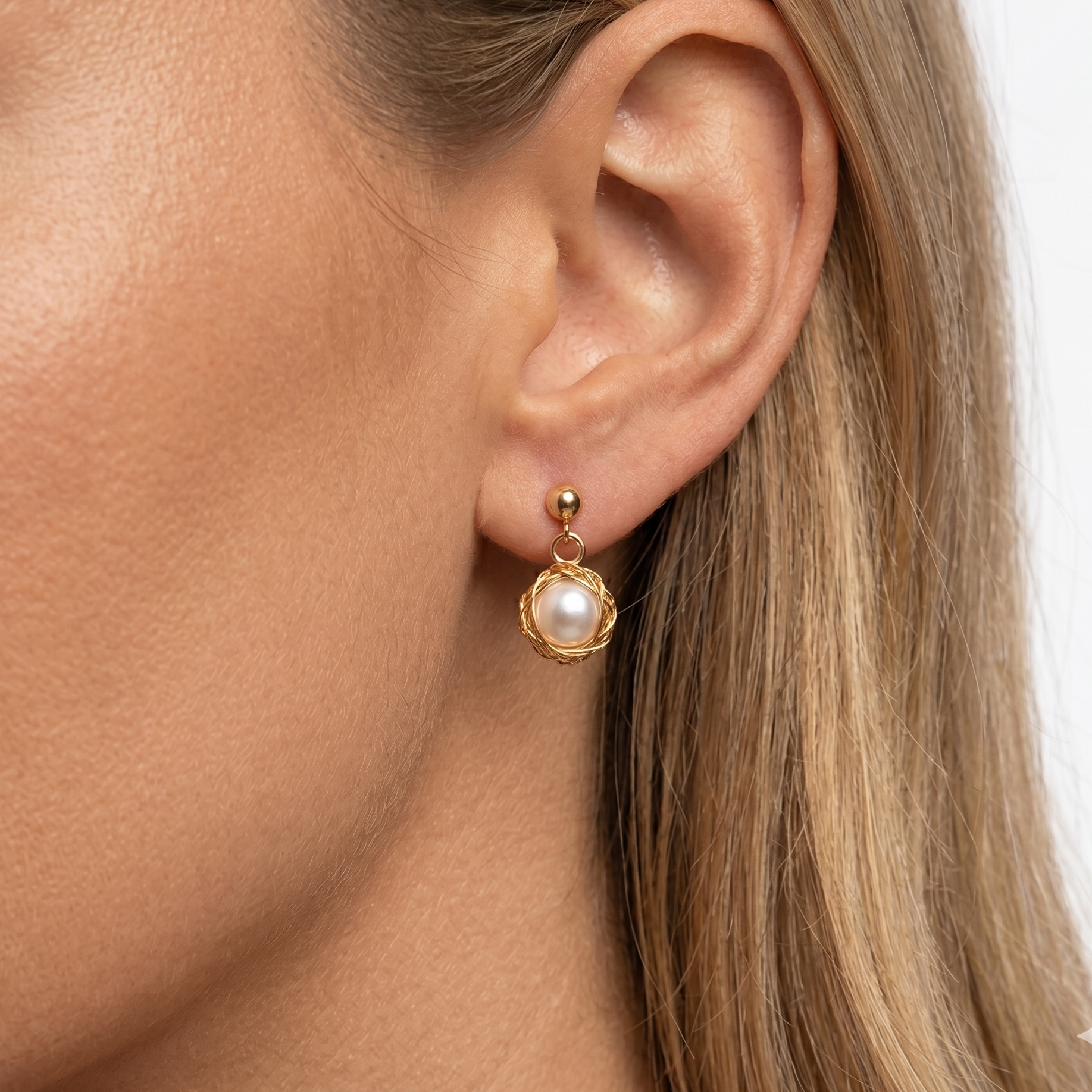 Gold earring with pearl detail worn by a person with blonde hair.