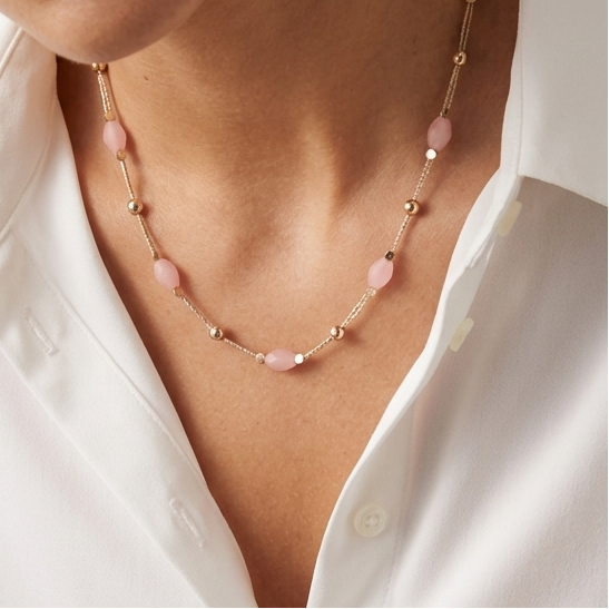 Woman wearing a pink beaded necklace with a white shirt against a neutral background