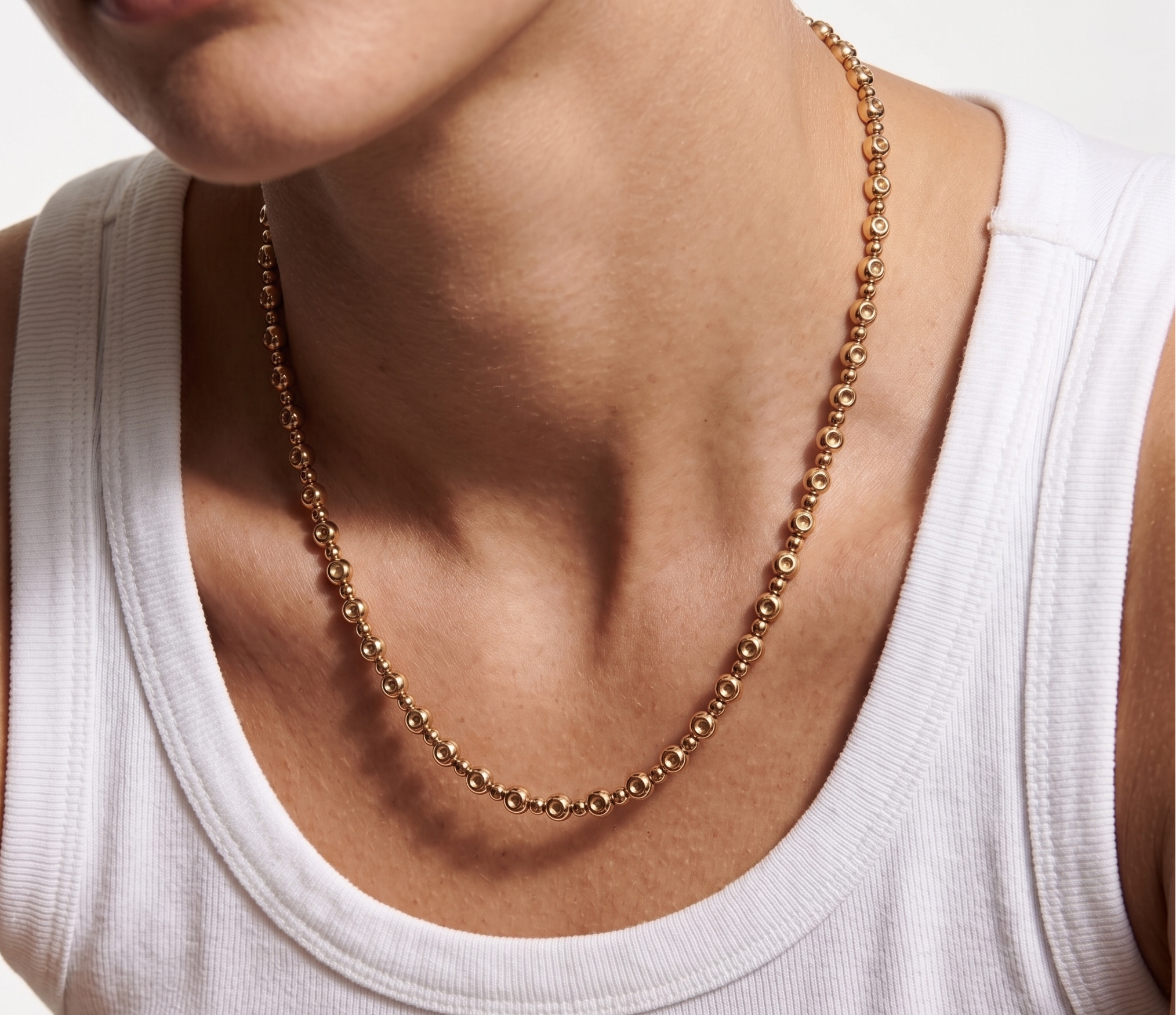 Gold necklace worn by a person in a white tank top on a neutral background