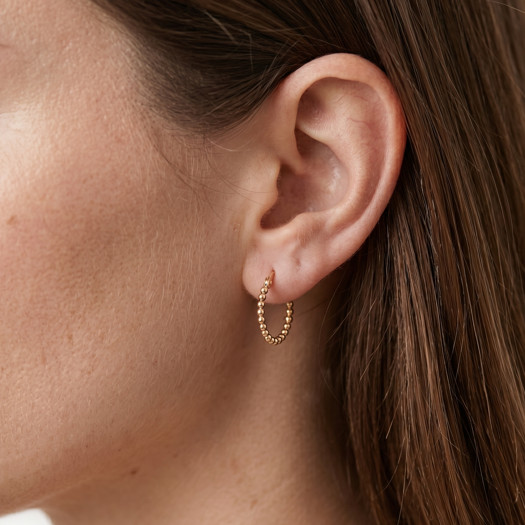 Close-up of a person wearing a gold hoop earring with a neutral background