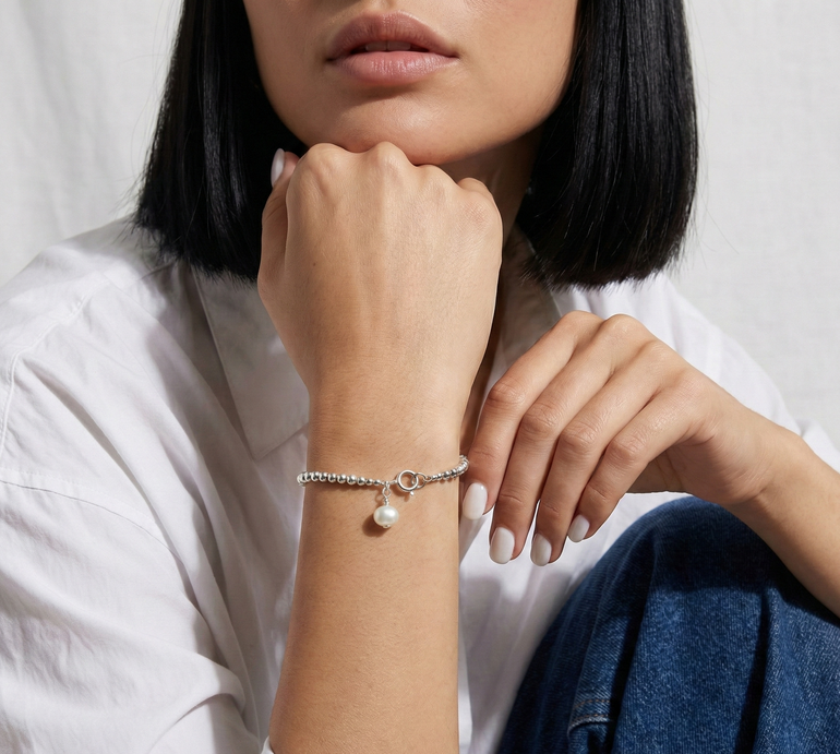 Person wearing a silver bracelet with a pearl on a plain background