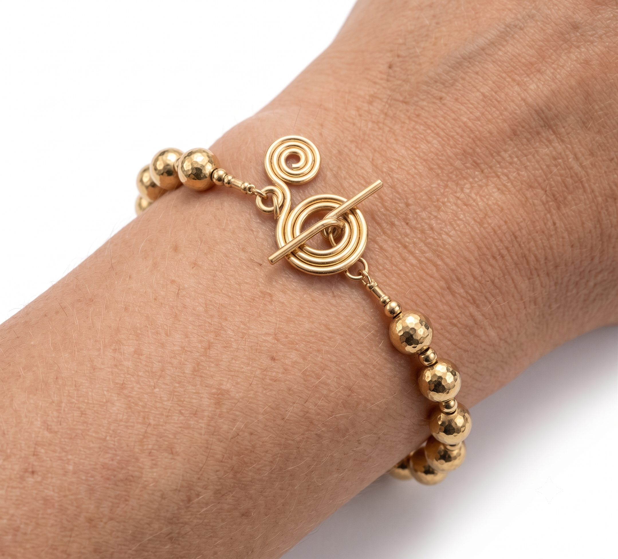 Gold bracelet with spherical beads and circular design on a wrist against a white background