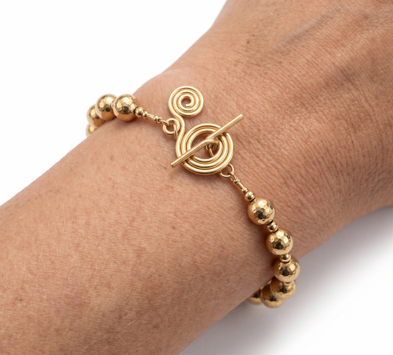 Gold bracelet with spherical beads and circular design on a wrist against a white background