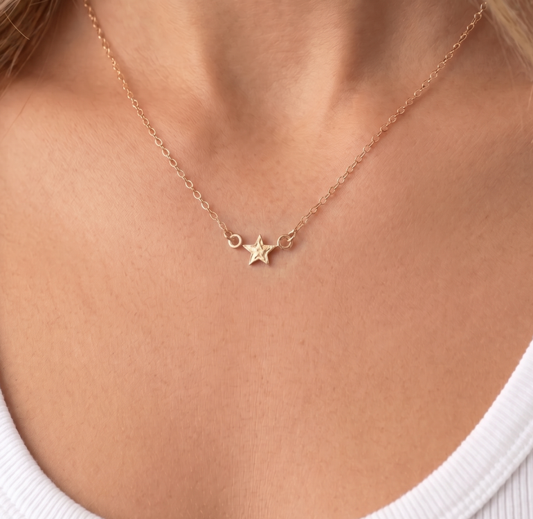 Rose gold necklace with star pendant on a person wearing a white top