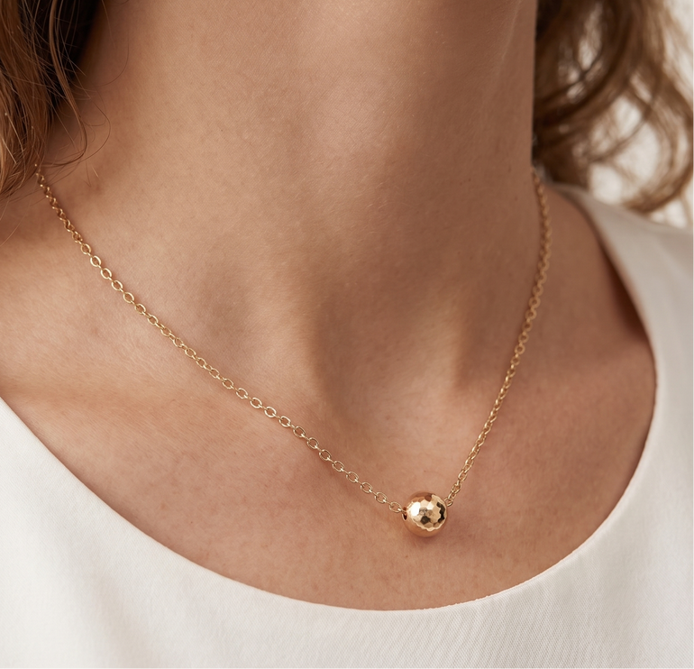 Gold necklace with a small round pendant worn by a person against a neutral background