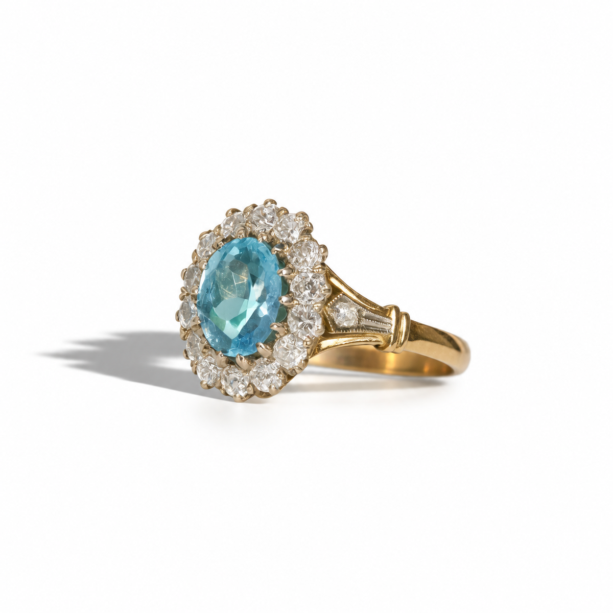 Vintage yellow gold ring featuring an oval blue gemstone surrounded by a halo of round diamonds, with diamond-set detailed shoulders.