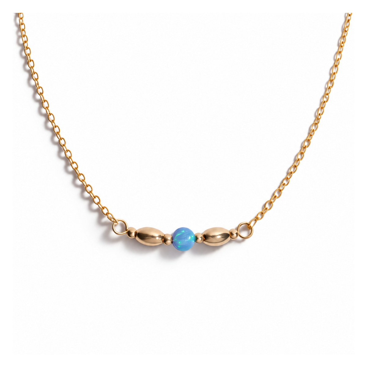 A delicate gold chain necklace featuring a central bar with two elongated gold beads flanking a small, round light blue bead, shown against a plain white background.