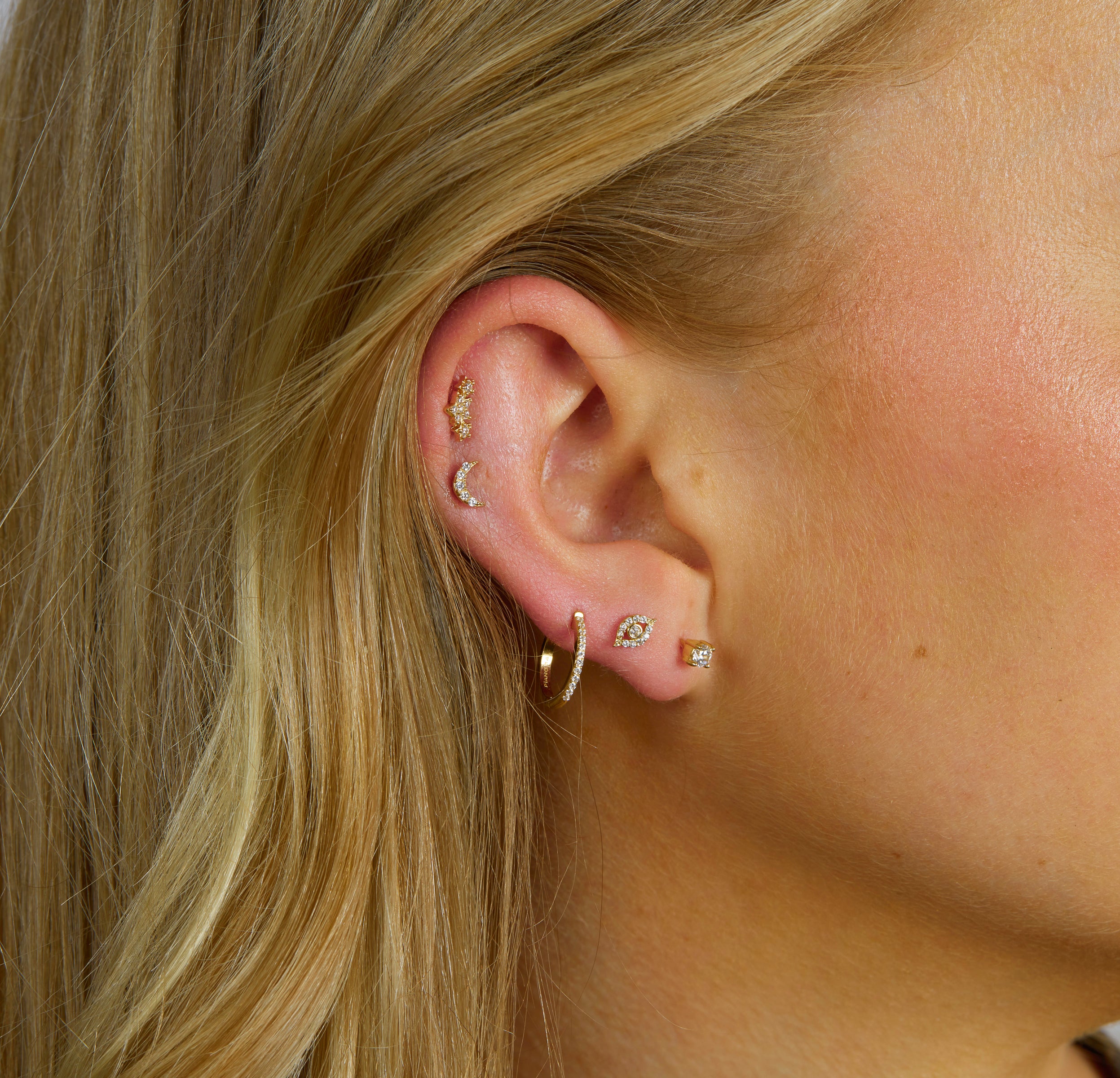 IMAGE CLOSE UP OF AN EAR STACKED WITH GOLD FLATBACK STUDS AND ONE CZ HOOP