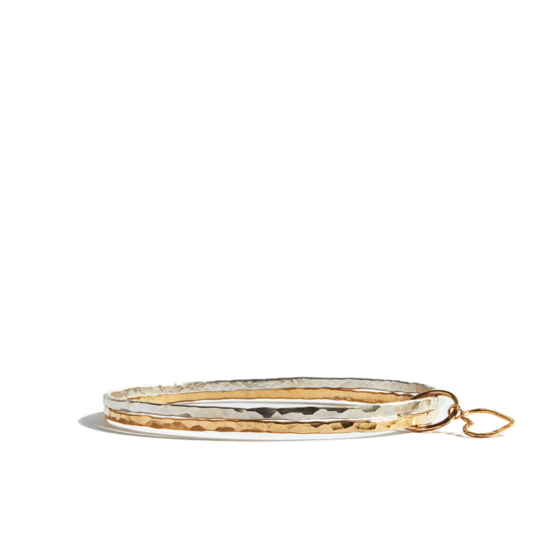 This stylish yellow gold and silver bangle is expertly hand-hammered and features a 14ct gold filled heart charm adding a touch of elegance. Crafted from 14ct gold filled and sterling silver this bangle is sure to add a touch of sophistication to any ensemble.