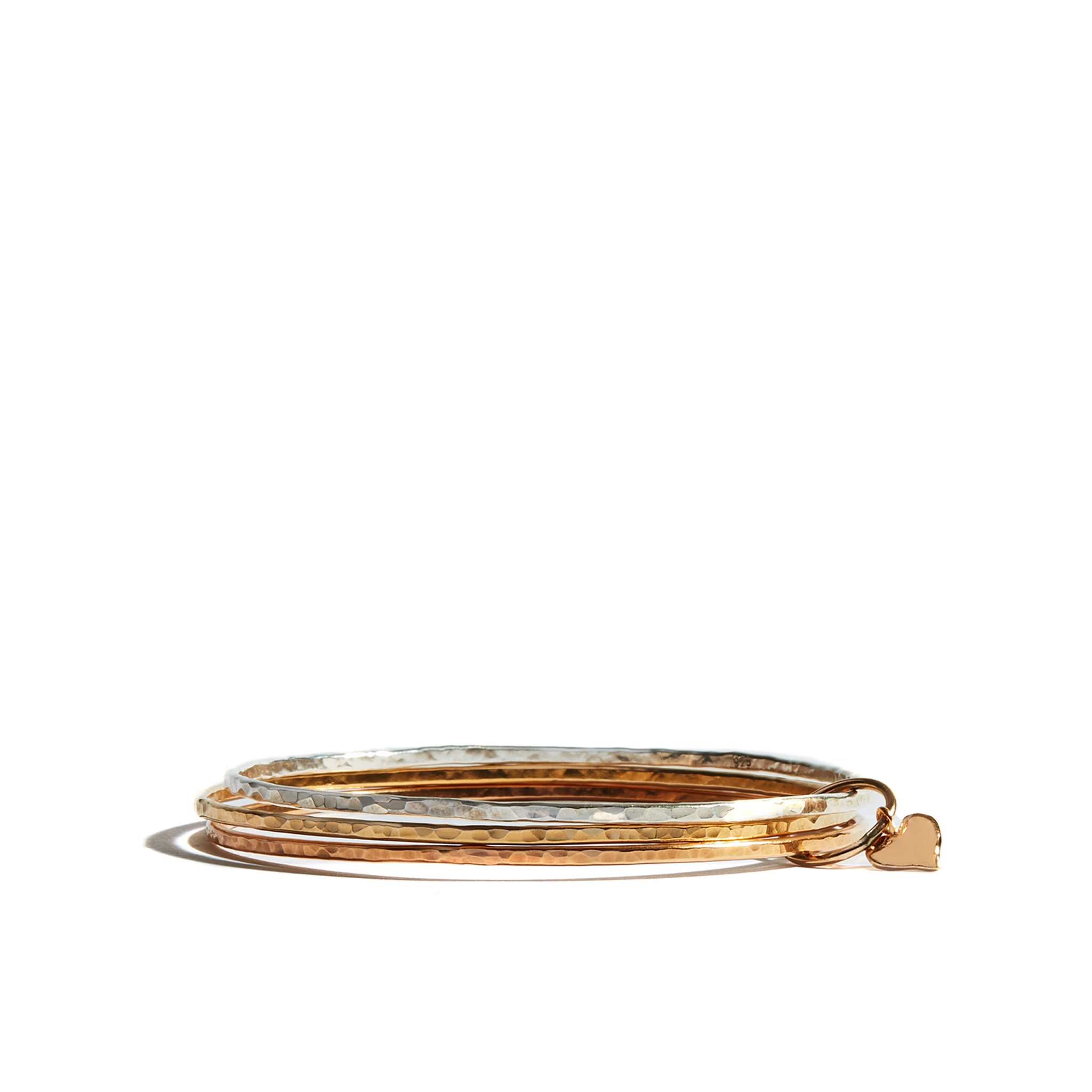 Expertly crafted from 14 carat gold filled the Three Tone Bangle is a beautiful work of art. Its carefully hand hammered finish creates an exquisite look and feel defined by its combination of yellow gold rose gold and silver. A playful heart charm completes the bangle offering a subtle touch of elegance.