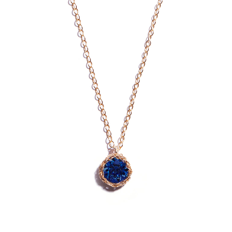 Close-up photo of a crochet necklace featuring a September birthstone pendant made of sapphire, set in 14 ct gold-filled metal.