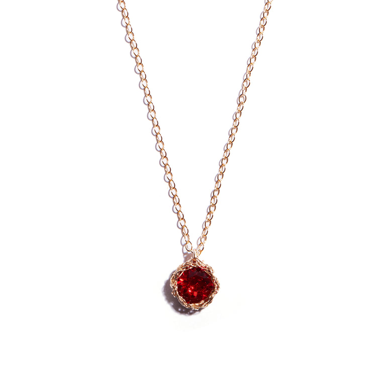 Close-up photo of a crochet necklace featuring a July birthstone pendant made of ruby, set in 14 ct gold-filled metal.