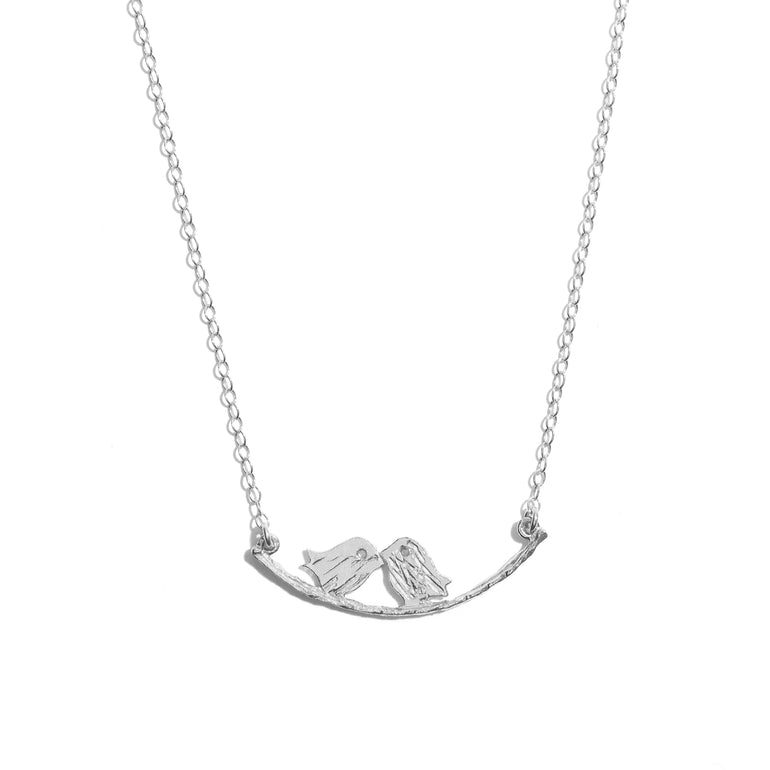 A silver necklace featuring a pendant with two birds sitting on a branch, with a lobster clasp, on a white background.