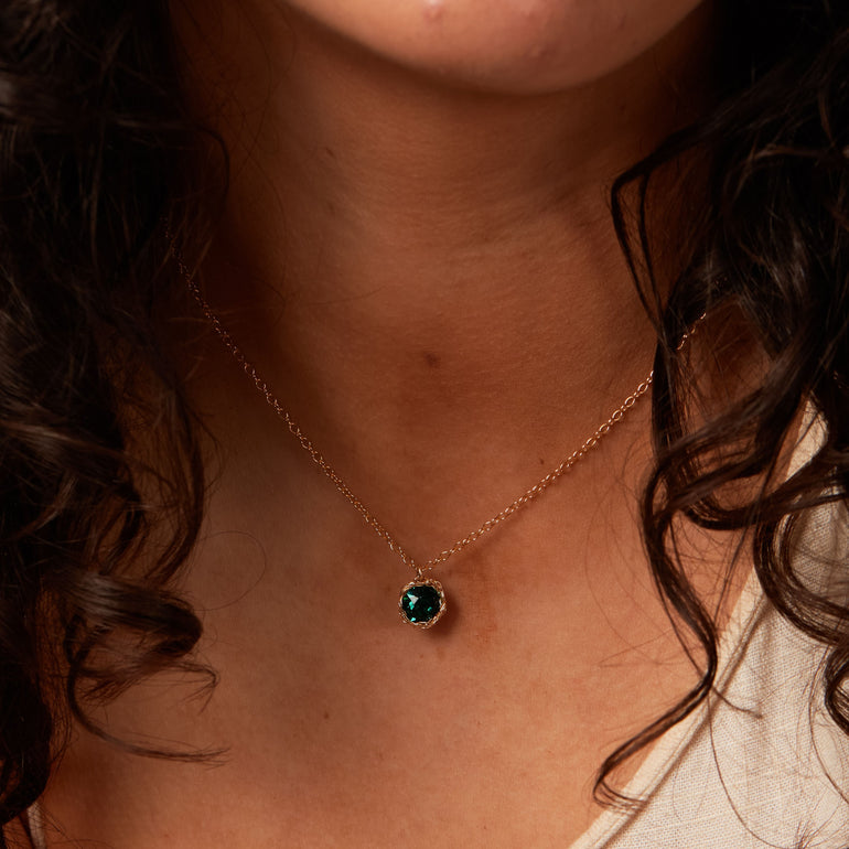 Close-up photo of a crochet necklace featuring a May birthstone pendant made of emerald, set in 14 ct gold-filled metal.