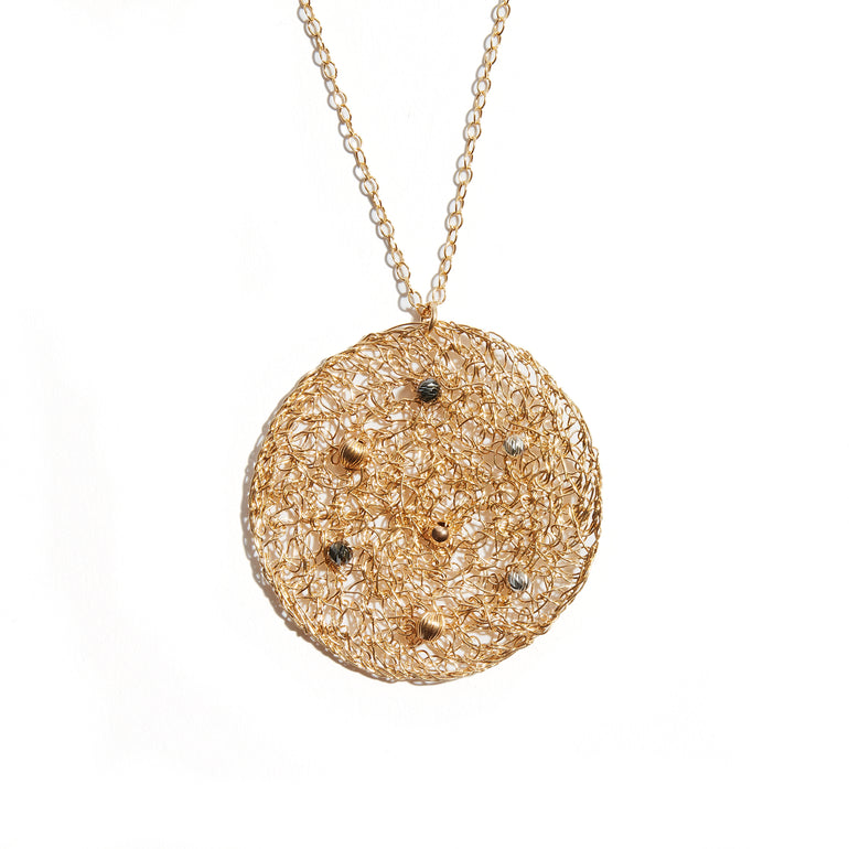 The Fí Night Sky Pendant is a large disc of intricately woven gold, complete with gorgeous twinkling little gems that mimic a clear night sky. The size and unique Fí design of this pendant makes it a wonderful statement piece.